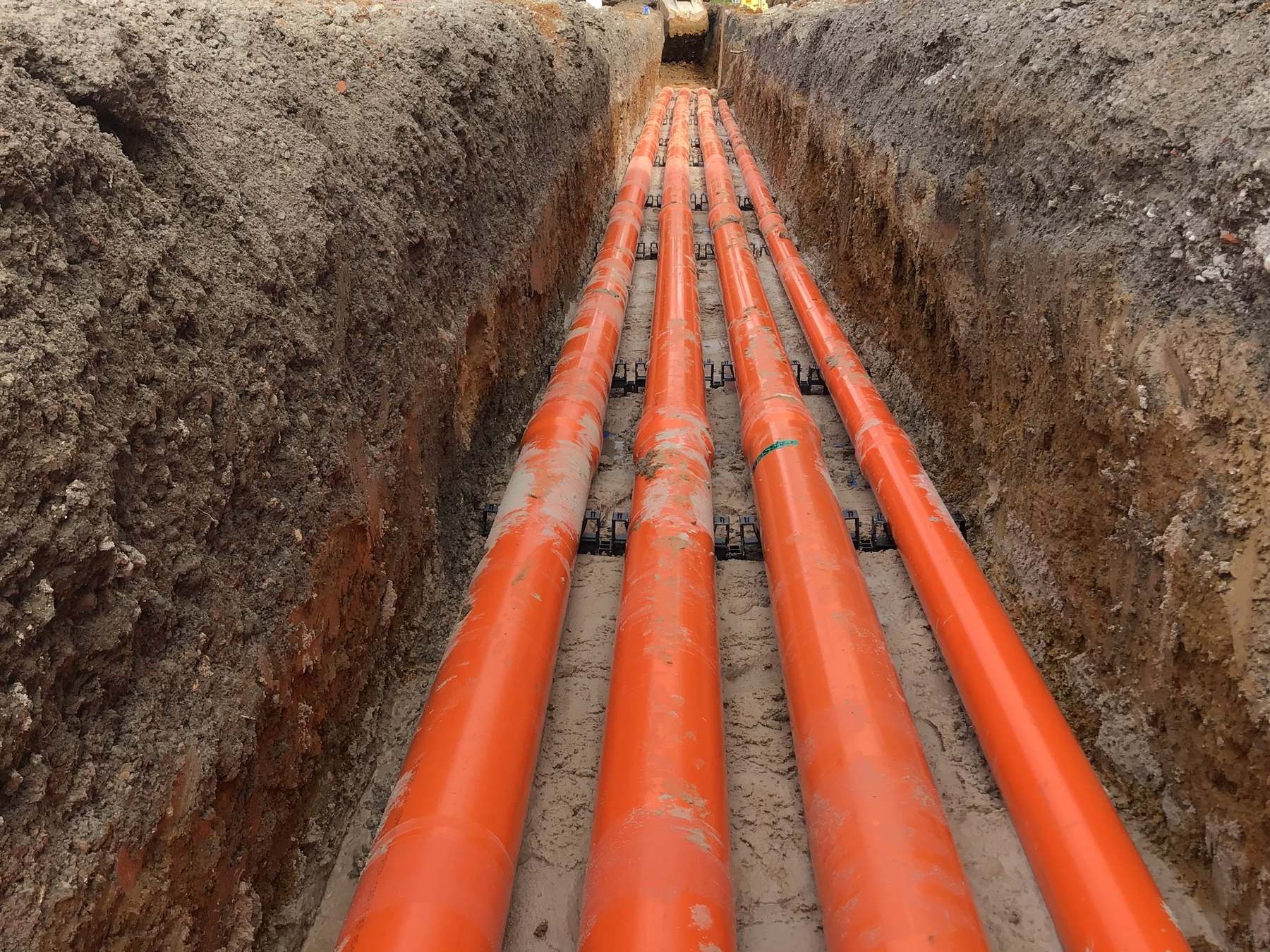 Bank of orange electrical conduits laid in an open trench on a JPR civil project