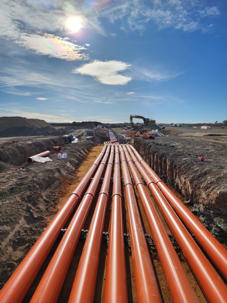 Bank of orange electrical conduits running along an open trench towards the horizon on a JPR civil project